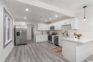 Kitchen with sink, white cabinets, kitchen peninsula, light hardwood / wood-style flooring, and appliances with stainless steel finishes