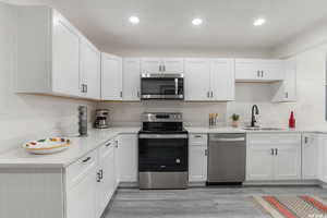 Kitchen with light wood-type flooring, white cabinetry, appliances with stainless steel finishes, and sink