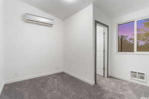 Empty room with lofted ceiling, dark colored carpet, and a wall mounted AC