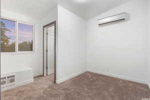 Carpeted empty room featuring lofted ceiling and a wall mounted air conditioner