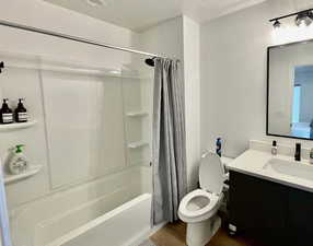 Full bathroom featuring shower / bathtub combination with curtain, vanity, a textured ceiling, hardwood / wood-style flooring, and toilet