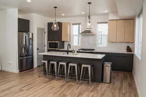 Kitchen with light brown cabinets, an island with sink, pendant lighting, island range hood, and appliances with stainless steel finishes