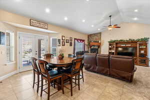 Tiled dining space with french doors, ceiling fan, a fireplace, and vaulted ceiling