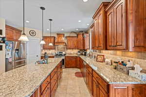 Kitchen featuring a center island, decorative light fixtures, appliances with stainless steel finishes, premium range hood, and light tile patterned flooring