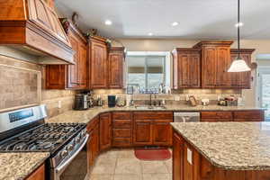 Kitchen featuring custom range hood, backsplash, stainless steel appliances, and sink