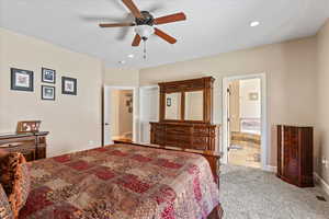 Carpeted bedroom featuring connected bathroom and ceiling fan