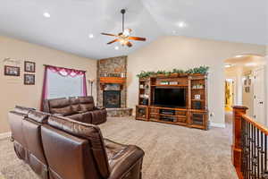 Carpeted living room with lofted ceiling, ceiling fan, and a fireplace