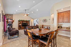 Dining space with a fireplace, vaulted ceiling, light tile patterned flooring, and ceiling fan