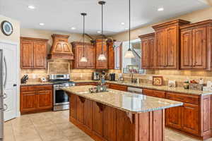 Kitchen with hanging light fixtures, a center island, appliances with stainless steel finishes, premium range hood, and a breakfast bar area