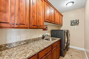 Clothes washing area with a textured ceiling, cabinets, independent washer and dryer, and sink