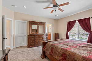 Bedroom with ceiling fan, connected bathroom, and light carpet