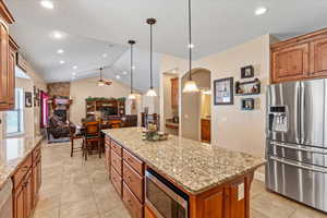 Kitchen featuring a fireplace, stainless steel appliances, a kitchen island, ceiling fan, and vaulted ceiling