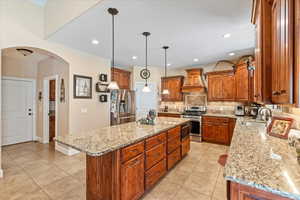 Kitchen with custom range hood, a center island, stainless steel appliances, sink, and light stone counters