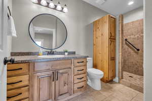 Bathroom with tiled shower, vanity, toilet, and tile patterned flooring