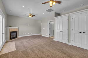 Master suite featuring ceiling fan, a textured ceiling, light carpet, and a tile fireplace