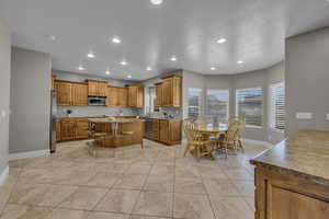 Kitchen featuring a kitchen island, light tile patterned floors, stainless steel appliances, a textured ceiling, and a kitchen bar