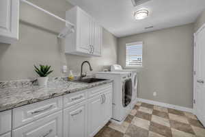 Washroom with washing machine and clothes dryer, a textured ceiling, cabinets, and sink