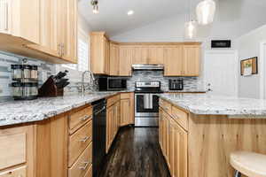 Kitchen featuring lofted ceiling, light brown cabinets, appliances with stainless steel finishes, and backsplash