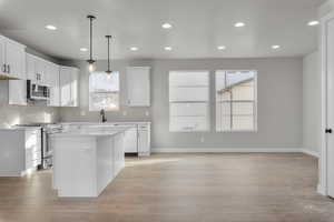 Kitchen with white cabinets, a kitchen island, appliances with stainless steel finishes, and light hardwood / wood-style flooring