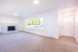 Unfurnished living room with light colored carpet and a stone fireplace