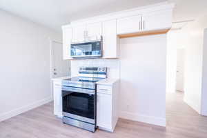 Kitchen featuring white cabinets, stainless steel appliances, decorative backsplash, and light hardwood / wood-style flooring