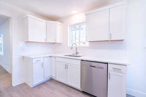 Kitchen with light wood-type flooring, sink, white cabinetry, decorative backsplash, and stainless steel dishwasher