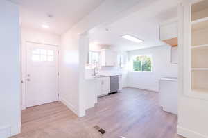 Interior space featuring light hardwood / wood-style floors, white cabinetry, dishwasher, and sink