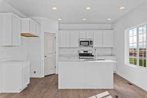 Kitchen featuring white cabinets, an island with sink, stainless steel appliances, and plenty of natural light