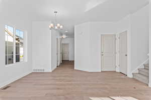 Empty room with a notable chandelier and light wood-type flooring