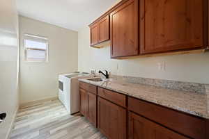 Washroom featuring washer and clothes dryer, cabinets, light wood-type flooring, and sink