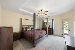 Bedroom with light colored carpet, ceiling fan, a raised ceiling, and access to exterior