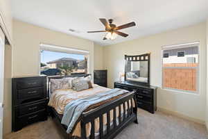 Bedroom with ceiling fan, light colored carpet, and a closet