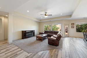 Living room with light hardwood / wood-style floors, a raised ceiling, a fireplace, and ceiling fan