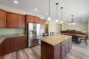 Kitchen with light stone counters, light wood-type flooring, decorative light fixtures, stainless steel refrigerator with ice dispenser, and a chandelier