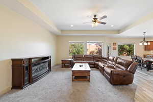 Living room featuring ceiling fan with notable chandelier, a raised ceiling, light hardwood / wood-style flooring, and plenty of natural light