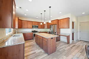 Kitchen with pendant lighting, light wood-type flooring, sink, a kitchen island, and stainless steel appliances