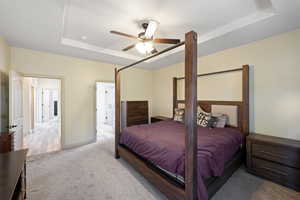 Carpeted bedroom featuring ceiling fan and a tray ceiling