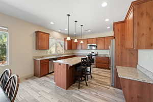 Kitchen featuring appliances with stainless steel finishes, a breakfast bar, light wood-type flooring, a center island, and sink