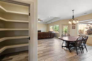 Dining area with ceiling fan with notable chandelier, light hardwood / wood-style floors, and a raised ceiling