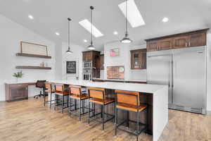 Kitchen featuring hanging light fixtures, light hardwood / wood-style flooring, built in appliances, lofted ceiling with skylight, and a breakfast bar