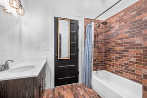 Bathroom with brick wall, vanity, and shower / bath combination with curtain