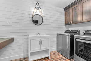 Laundry area featuring washer and clothes dryer, wood walls, and cabinets