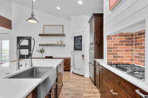 Kitchen featuring light hardwood / wood-style floors, lofted ceiling, hanging light fixtures, stainless steel appliances, and dark brown cabinetry