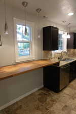 Kitchen featuring sink, stainless steel dishwasher, decorative light fixtures, backsplash, and wood counters