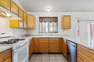 Kitchen featuring white gas stove, sink, kitchen peninsula, light tile patterned floors, and stainless steel dishwasher