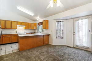 Kitchen featuring vaulted ceiling, kitchen peninsula, semi formal dining with french door, white stove, ceiling fan, and a healthy amount of sunlight