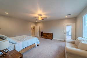 Bedroom with ensuite bath, ceiling fan, and light colored carpet