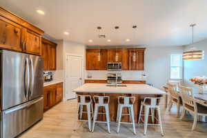 Kitchen with a kitchen bar, appliances with stainless steel finishes, hanging light fixtures, and a kitchen island with sink