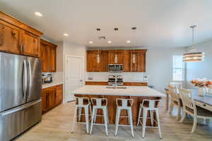 Kitchen with pendant lighting, a center island with sink, appliances with stainless steel finishes, and a kitchen bar