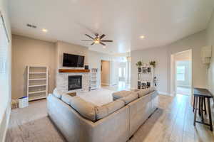 Living room featuring ceiling fan, a stone fireplace, and light wood-type flooring